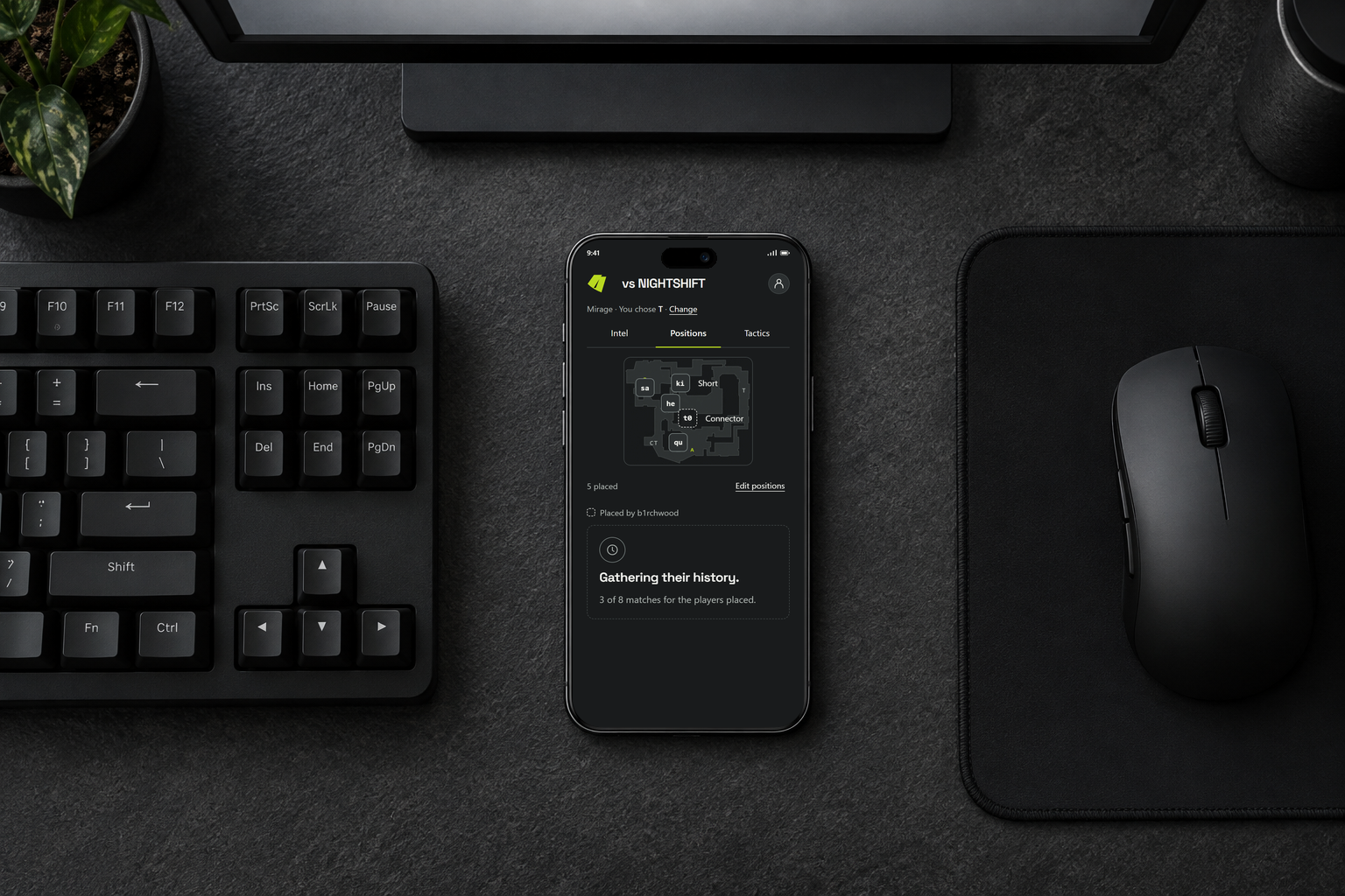 A phone lies flat beside a black keyboard on a charcoal desk, showing saved CT positions on Mirage under the glow of a monitor.